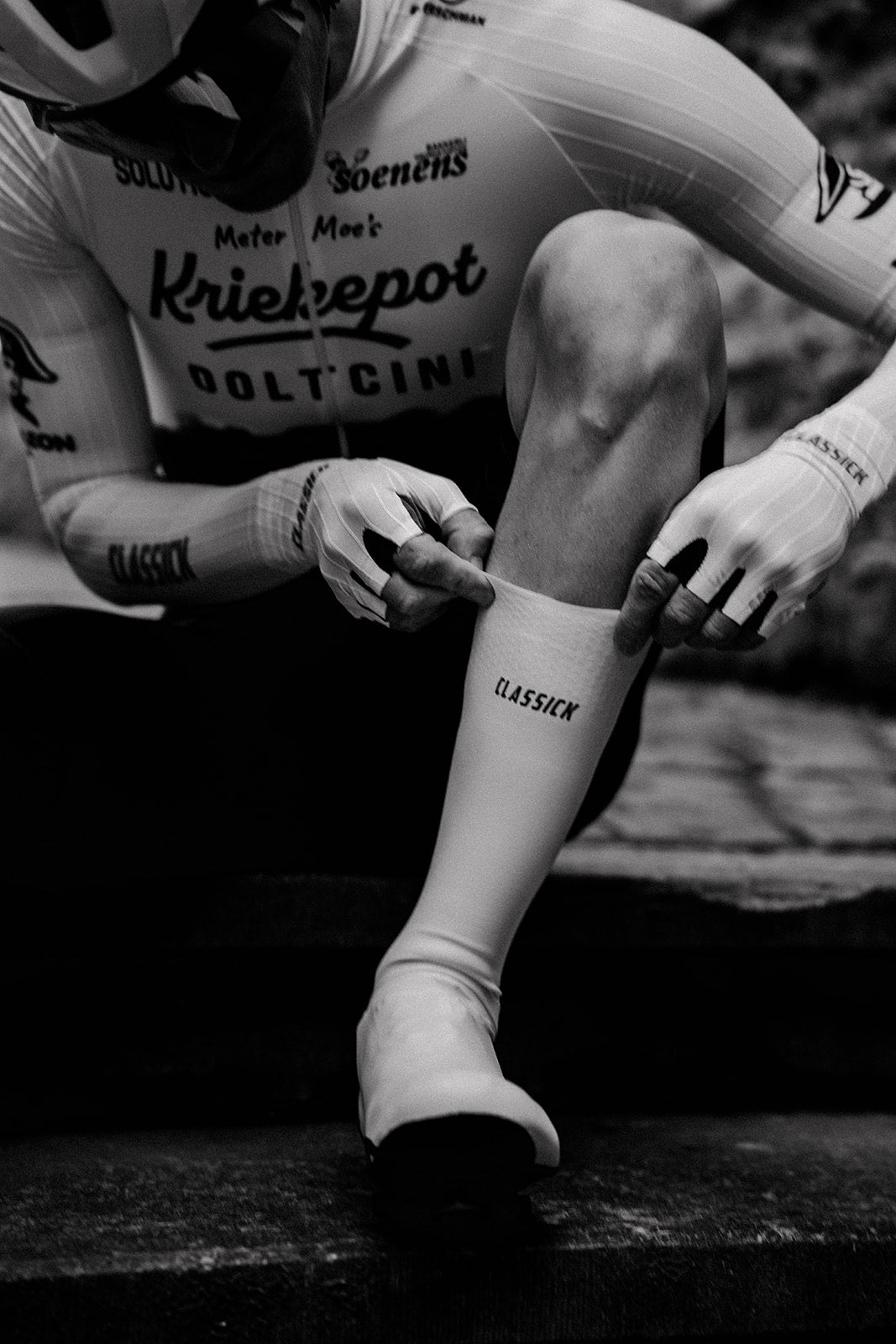 Een renner trekt witte Flandrien Shoe Covers aan op een buitentrap.